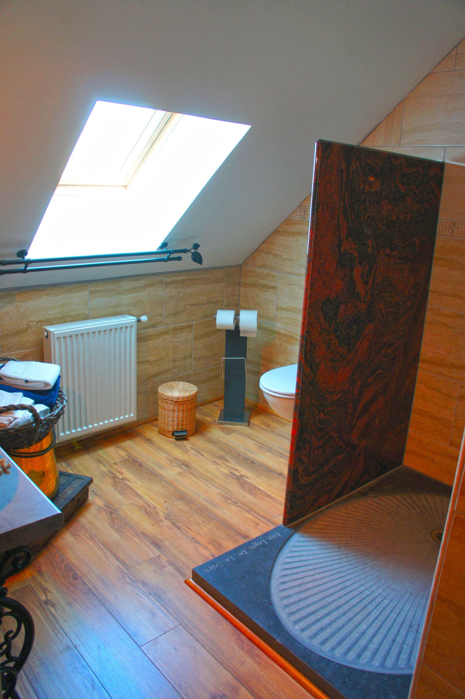 A modern bathroom with a skylight, wooden flooring, a radiator, a toilet, and a small trash bin.