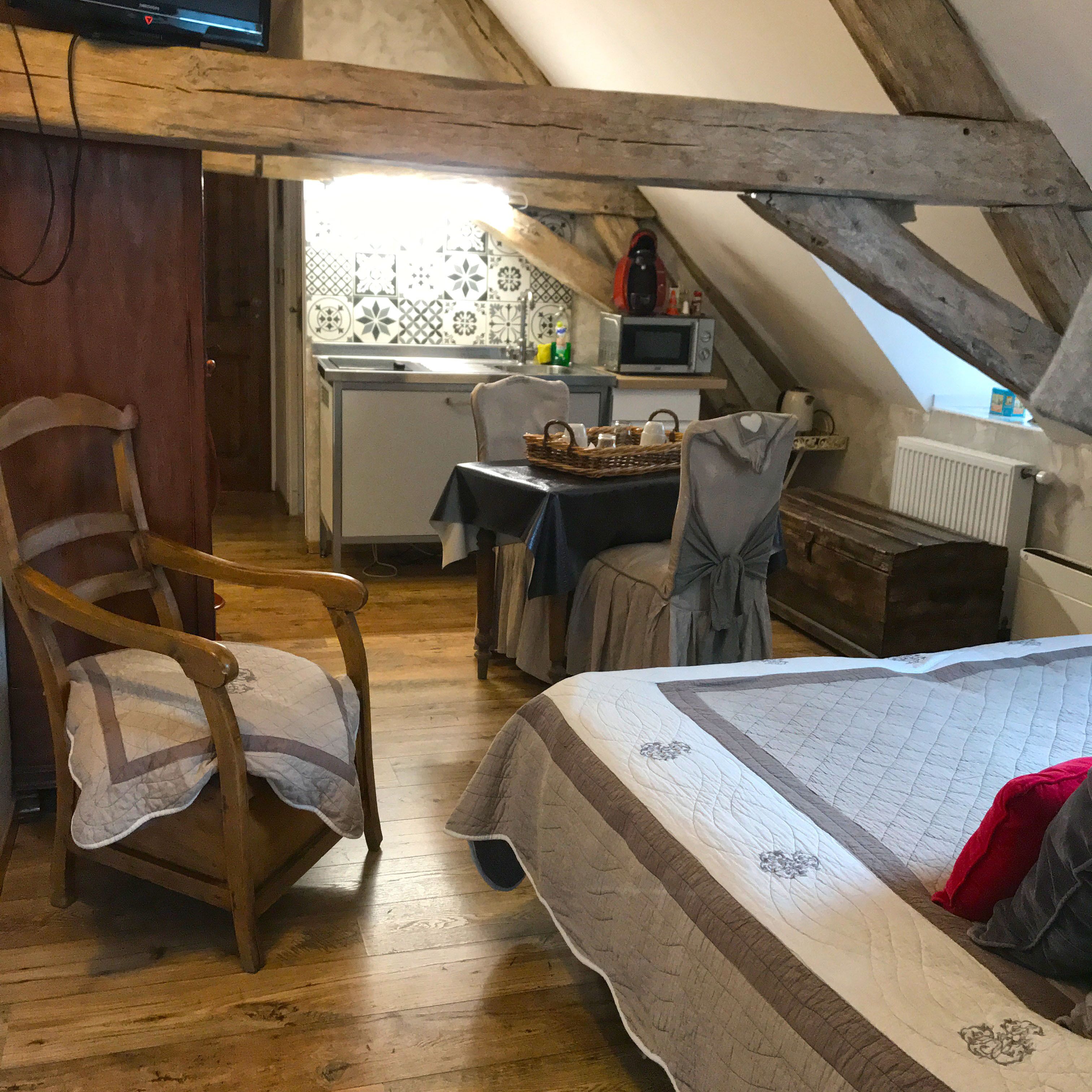 Ein gemütliches Schlafzimmer im Dachgeschoss mit einem Holzstuhl, einem Bett mit Quilzdecke, einem kleinen Tisch mit Korb und einer Küchenzeile mit Mikrowelle.