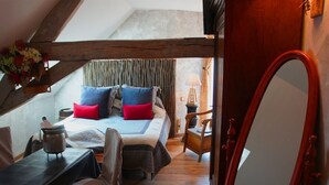 Une chambre confortable située dans les combles, avec un plafond en bois, un lit agrémenté de plusieurs coussins, une petite table avec une bouilloire et un miroir.