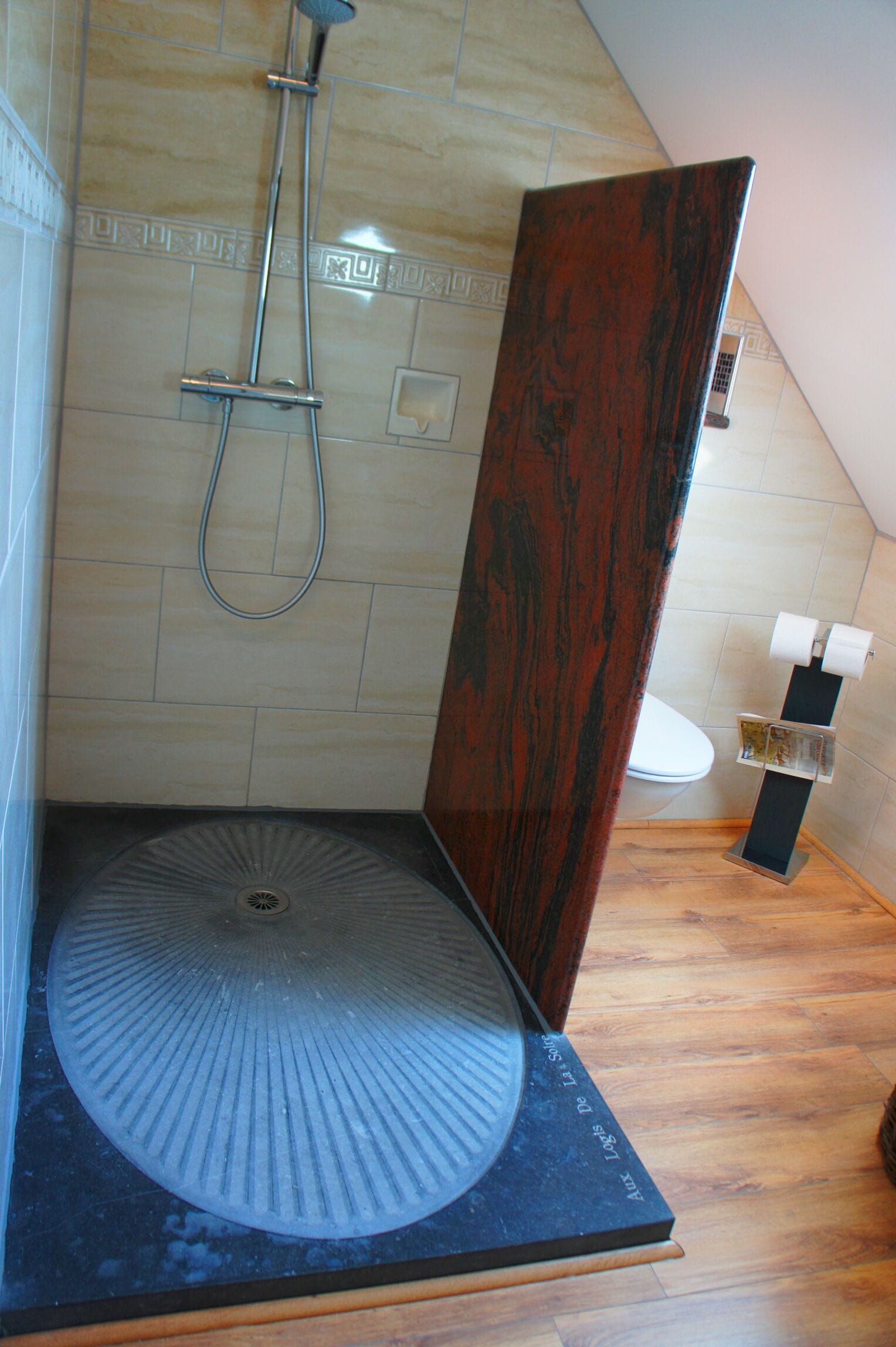 A shower with a circular floor, a wooden door, and a toilet with a paper holder.