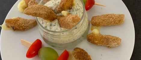 En hvid tallerken med en glas skål med dip, omgivet af panerede snacks og kirsebærtomater.