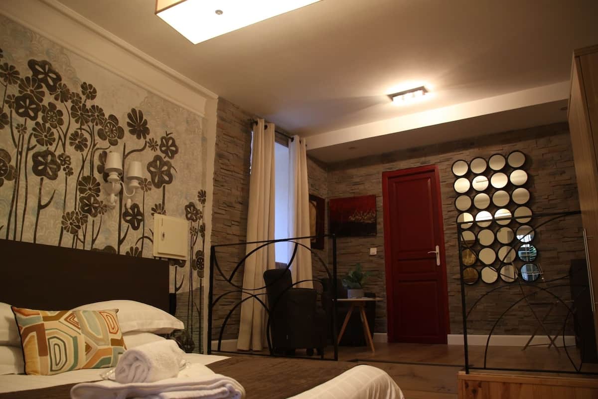 A hotel room with a bed, a chair, a red door, and a wall with circular mirrors.