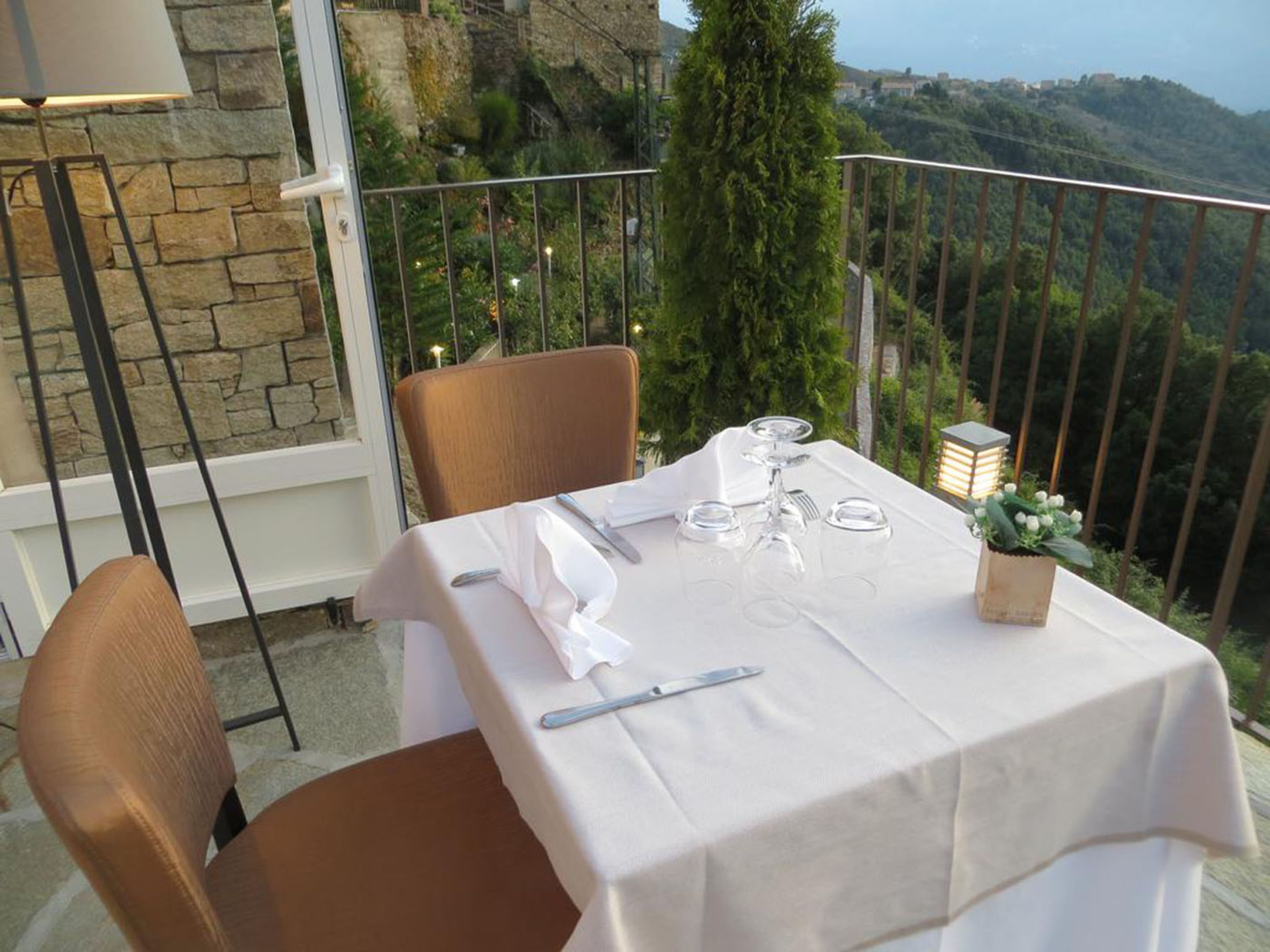 Mesa para cuatro dispuesta en un balcón, con un muro de piedra y vegetación al fondo.