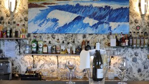 Zona de bar con un cuadro grande de olas, varias botellas de licor y vasos sobre el mostrador.