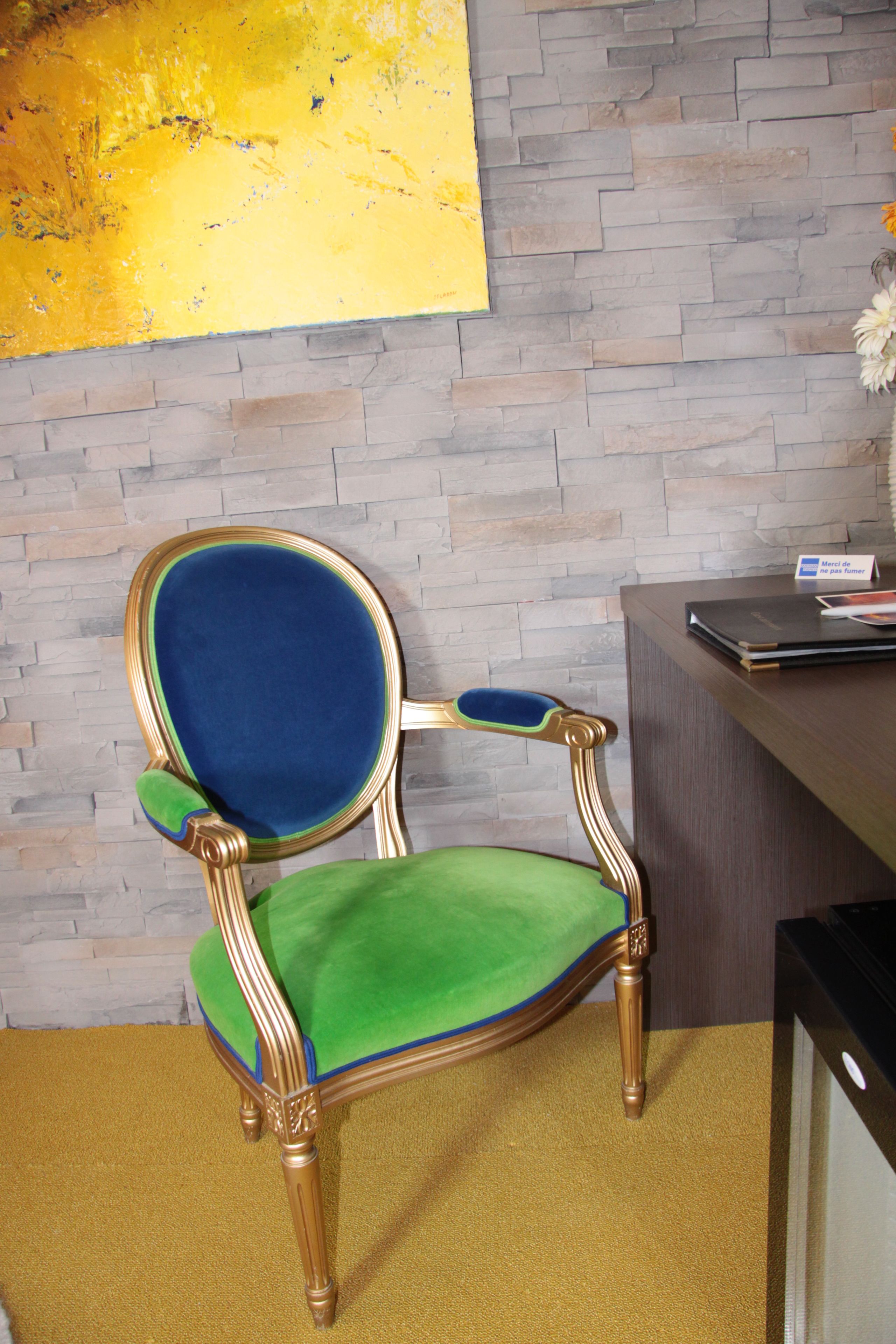 A chair with a green seat and blue backrest, positioned in front of a desk with a nameplate and a book.