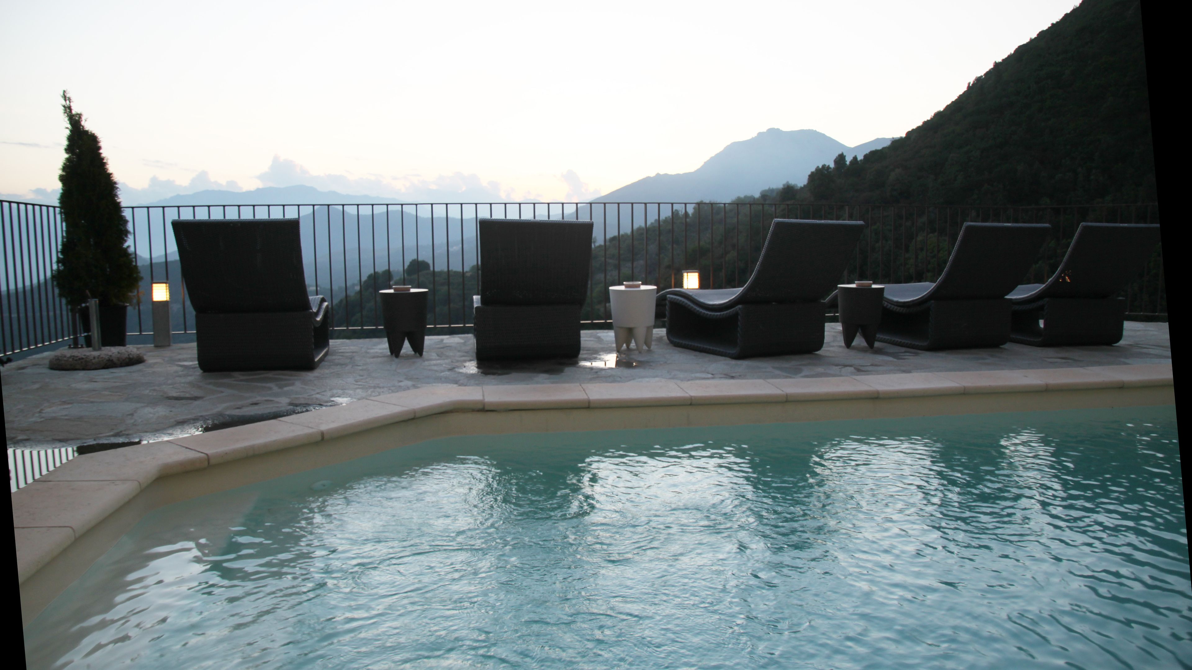 A poolside area with lounge chairs and tables, a small pool, and a mountainous backdrop.