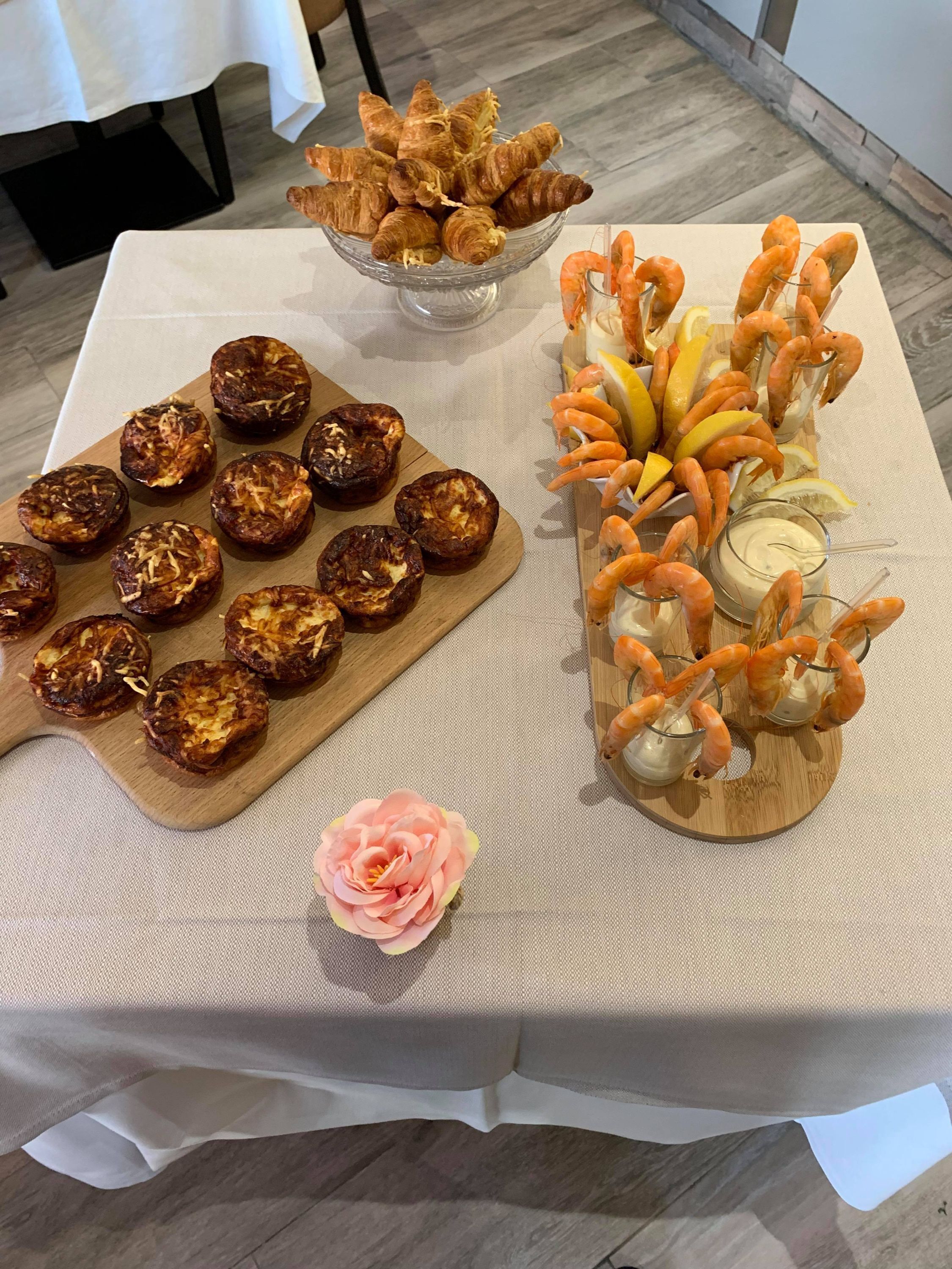 Une table avec différents aliments, notamment des croissants, des crevettes et une fleur décorative.
