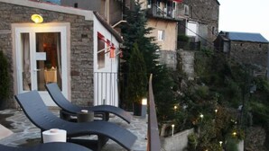 Un patio de piedra con sillones de descanso y barandilla con vistas a una colina.