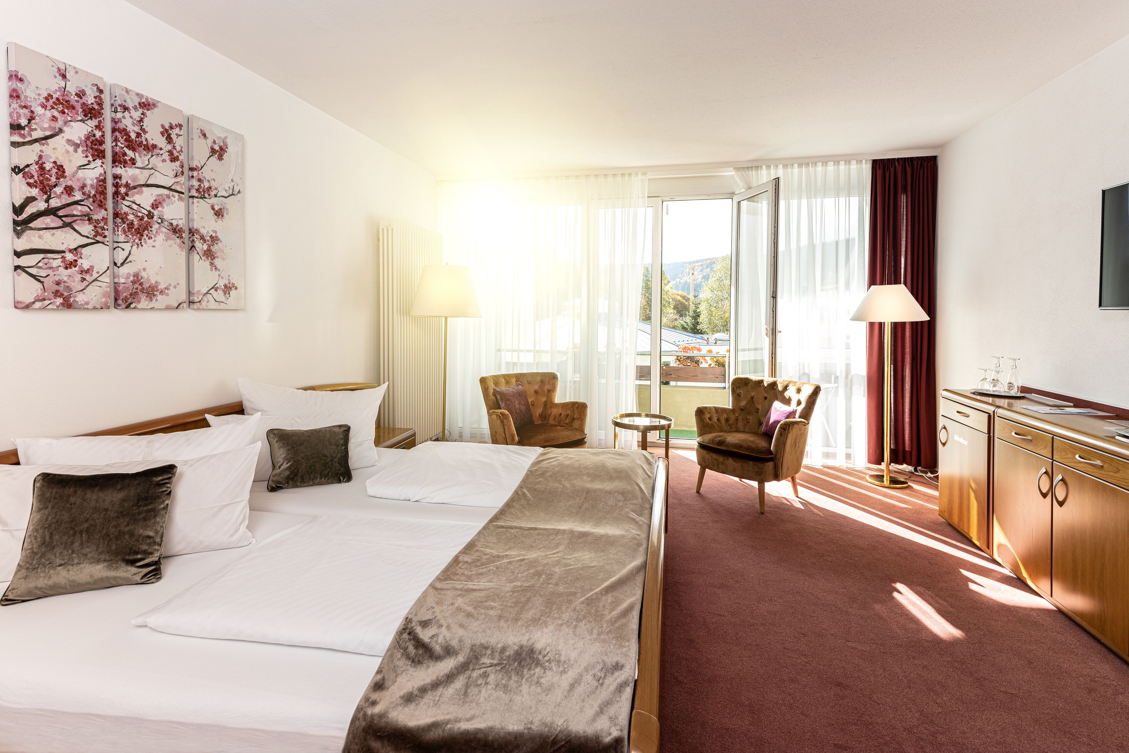 A hotel room with a large bed, two armchairs, a small table, a desk, and a painting on the wall.