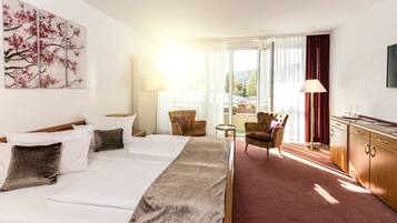 A hotel room with a large bed, two armchairs, a small table, a desk, and a painting on the wall.