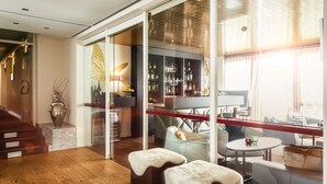 A modern living room with a glass partition, a bar area, and a staircase leading to another level. - Hotel Traube Revital (Wurmlingen)
