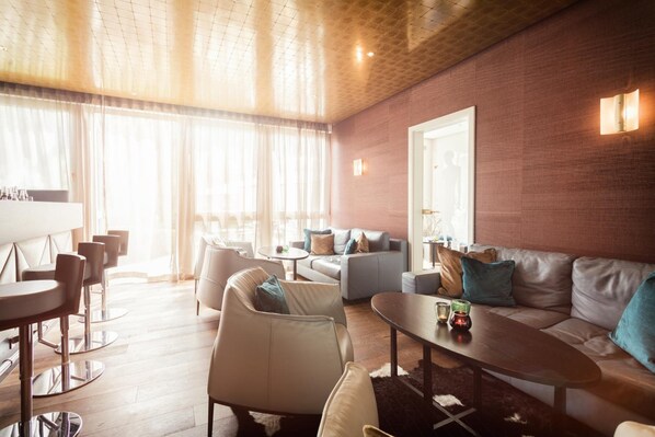 A modern living room with a brick wall, leather sofas, and a dining area with round tables and chairs. - Hotel Traube Revital (Wurmlingen)