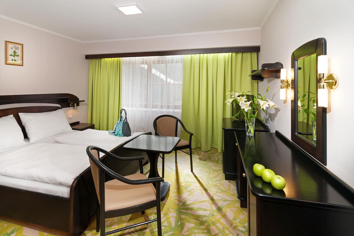 Quarto de hotel com cama, escrivaninha, cadeira, espelho e janela com cortinas.
