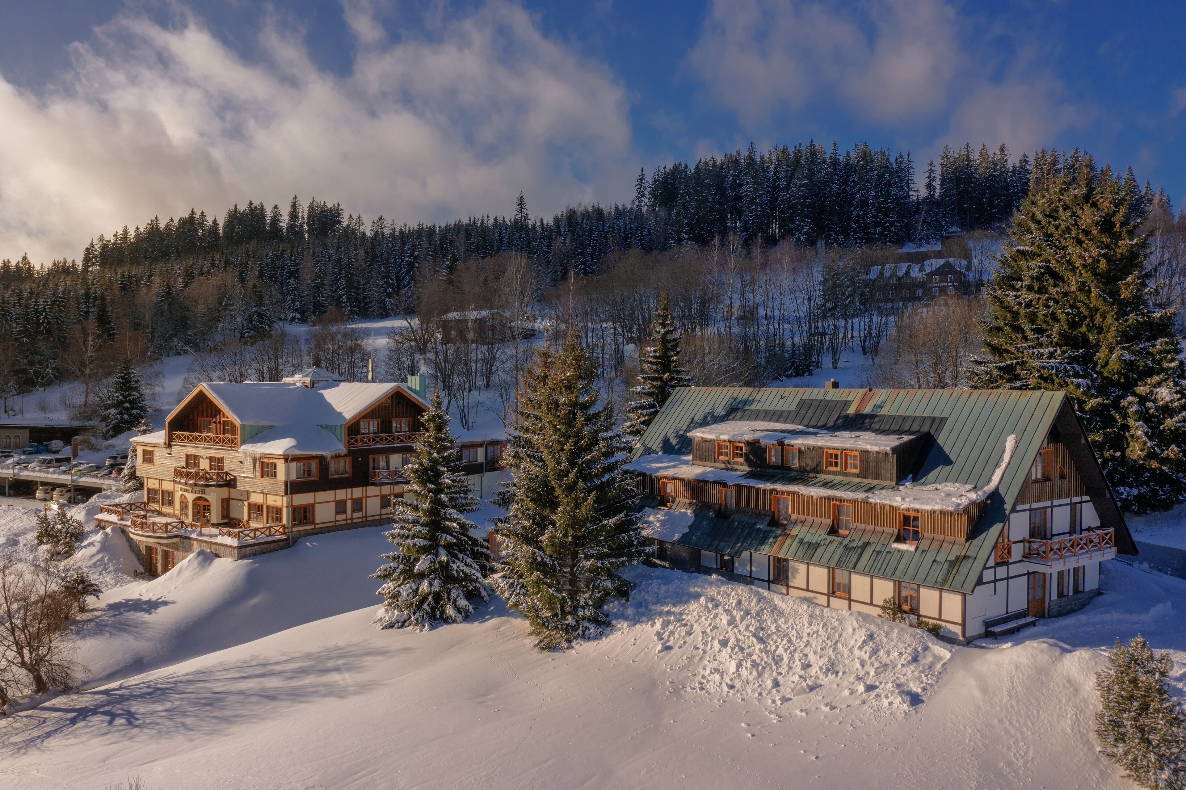 A large, multi-story lodge with a traditional Alpine architectural style, surrounded by snow-covered trees and a forested backdrop.
