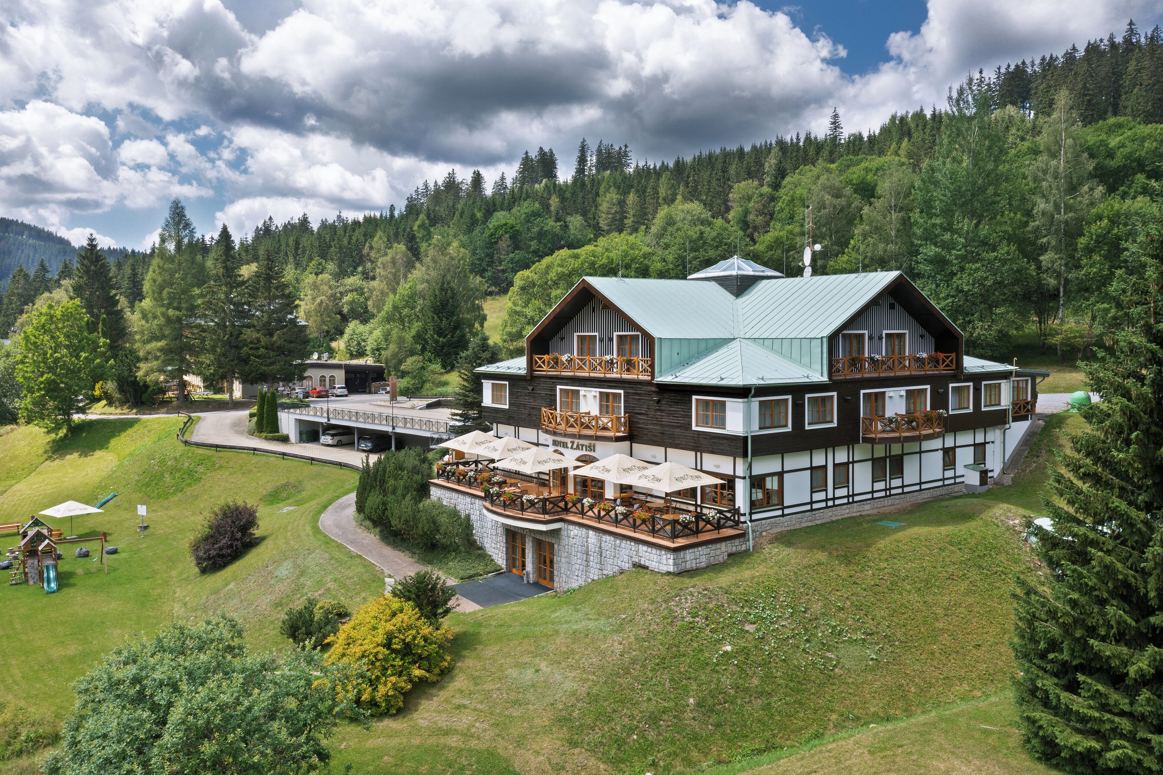A multi-story hotel with a balcony, stone foundation, and a view of a forested hillside.