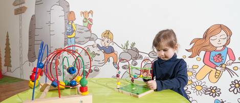 A child playing with a wooden toy on a green table in a room with a wall mural.