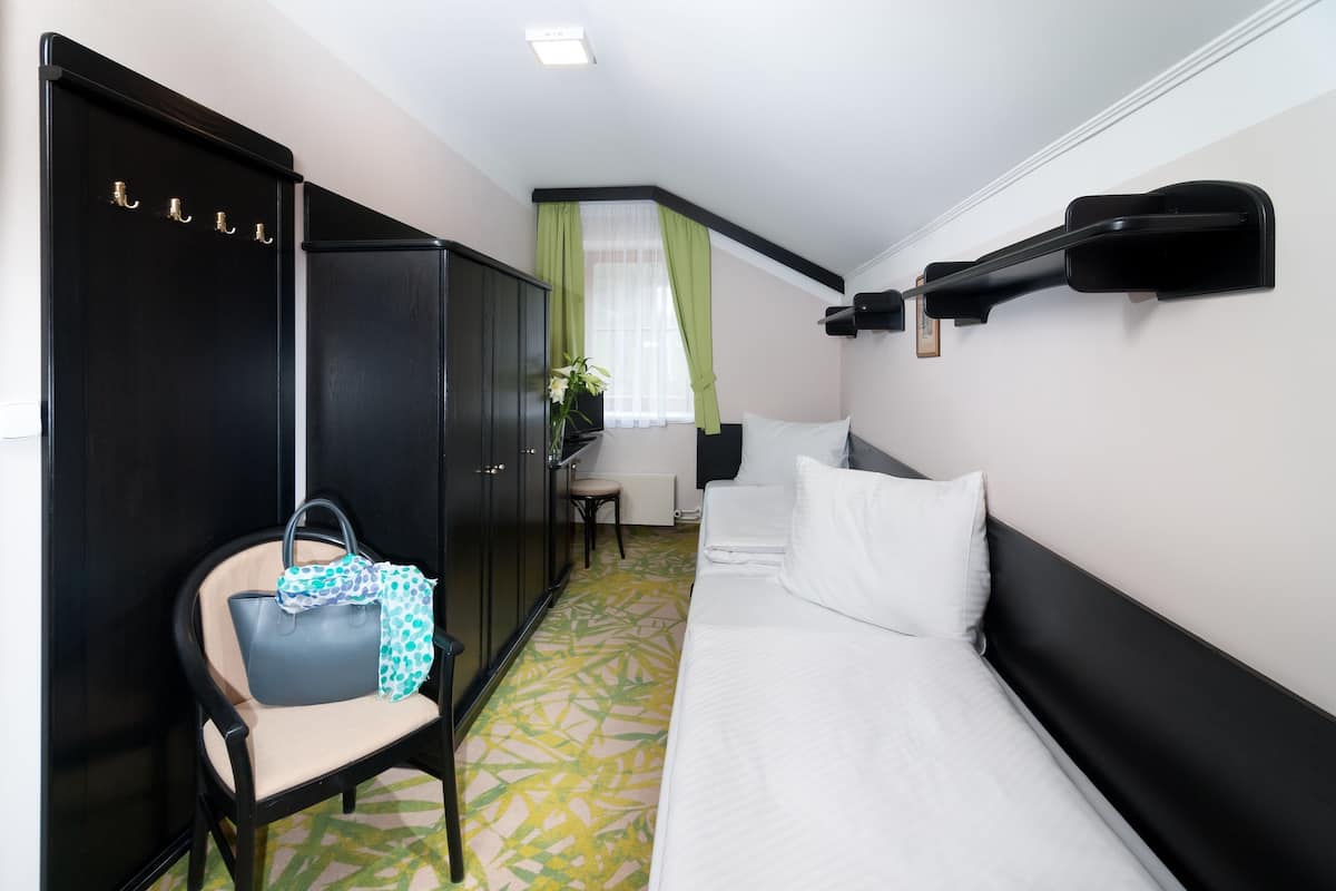 Quarto de hotel com cama, cadeira, guarda-roupa, escrivaninha e janela com cortinas.