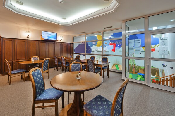 Un salón de conferencias con mobiliario de madera, una televisión y ventanas amplias con carteles educativos.