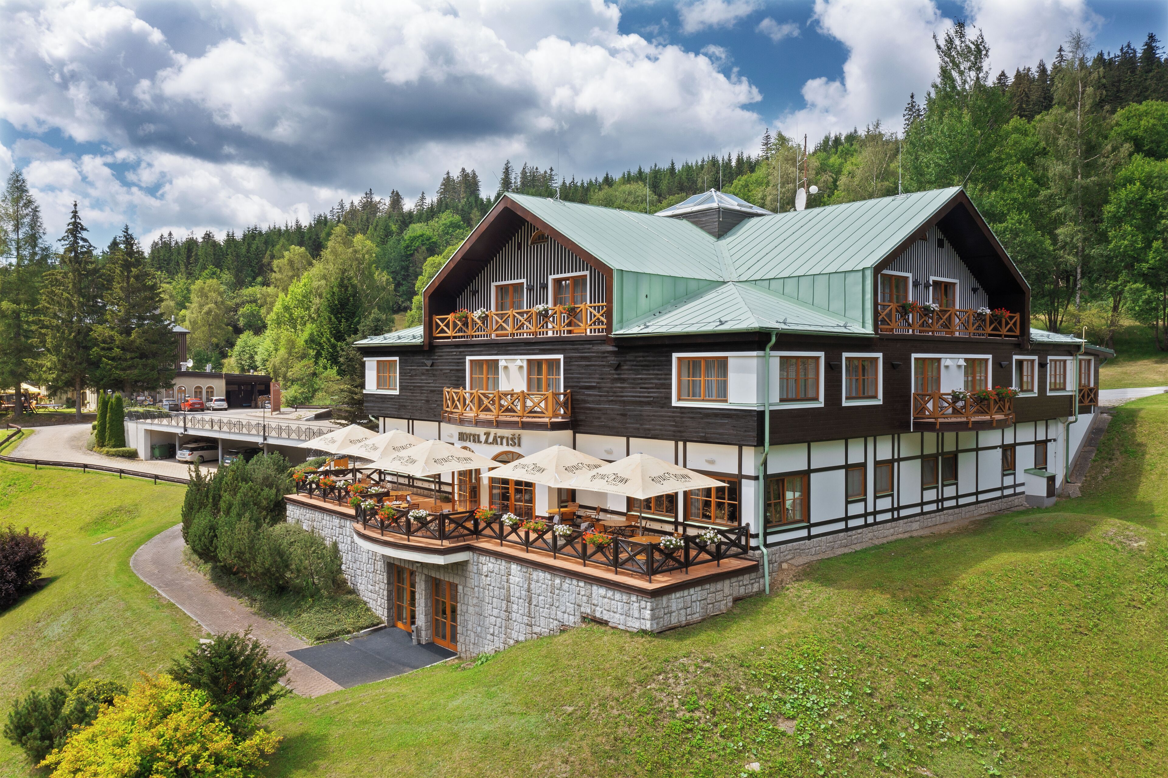 A large, two-story lodge with a green roof, wooden balconies, and outdoor seating areas.
