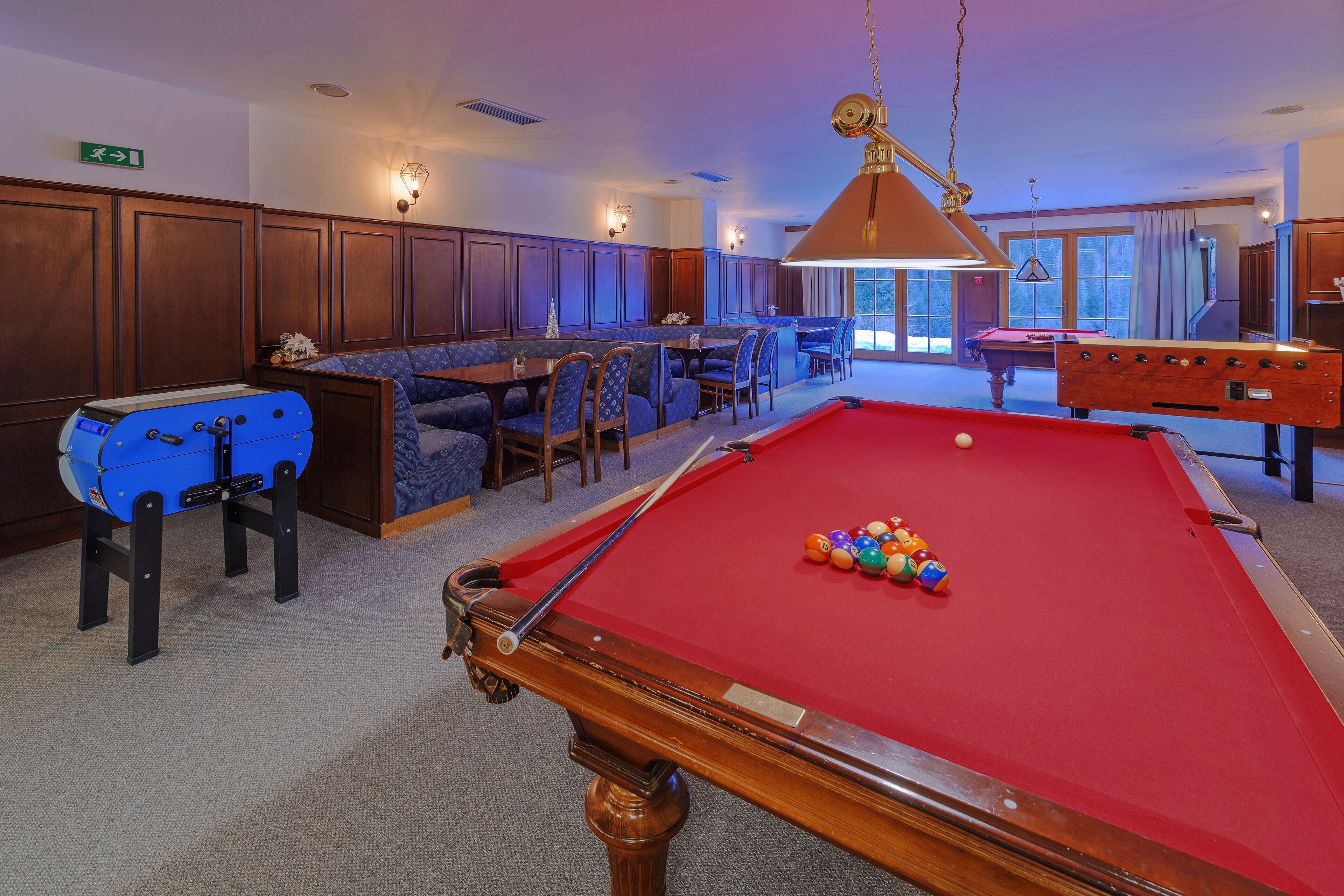 A pool table with balls, a blue foosball table, and a billiard cue.
