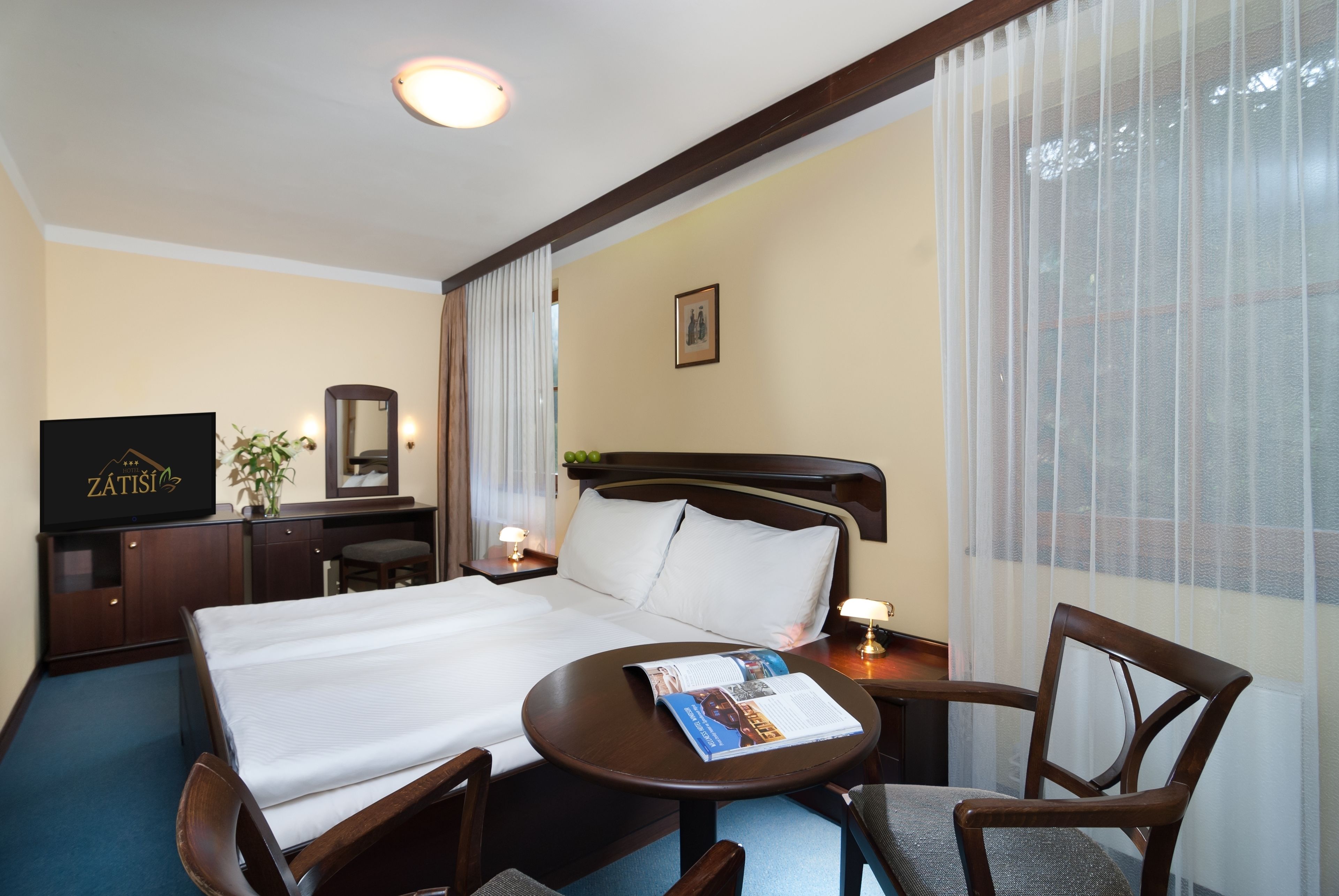 A hotel room with a large bed, a desk with a chair, a television, a mirror, and a window with curtains.