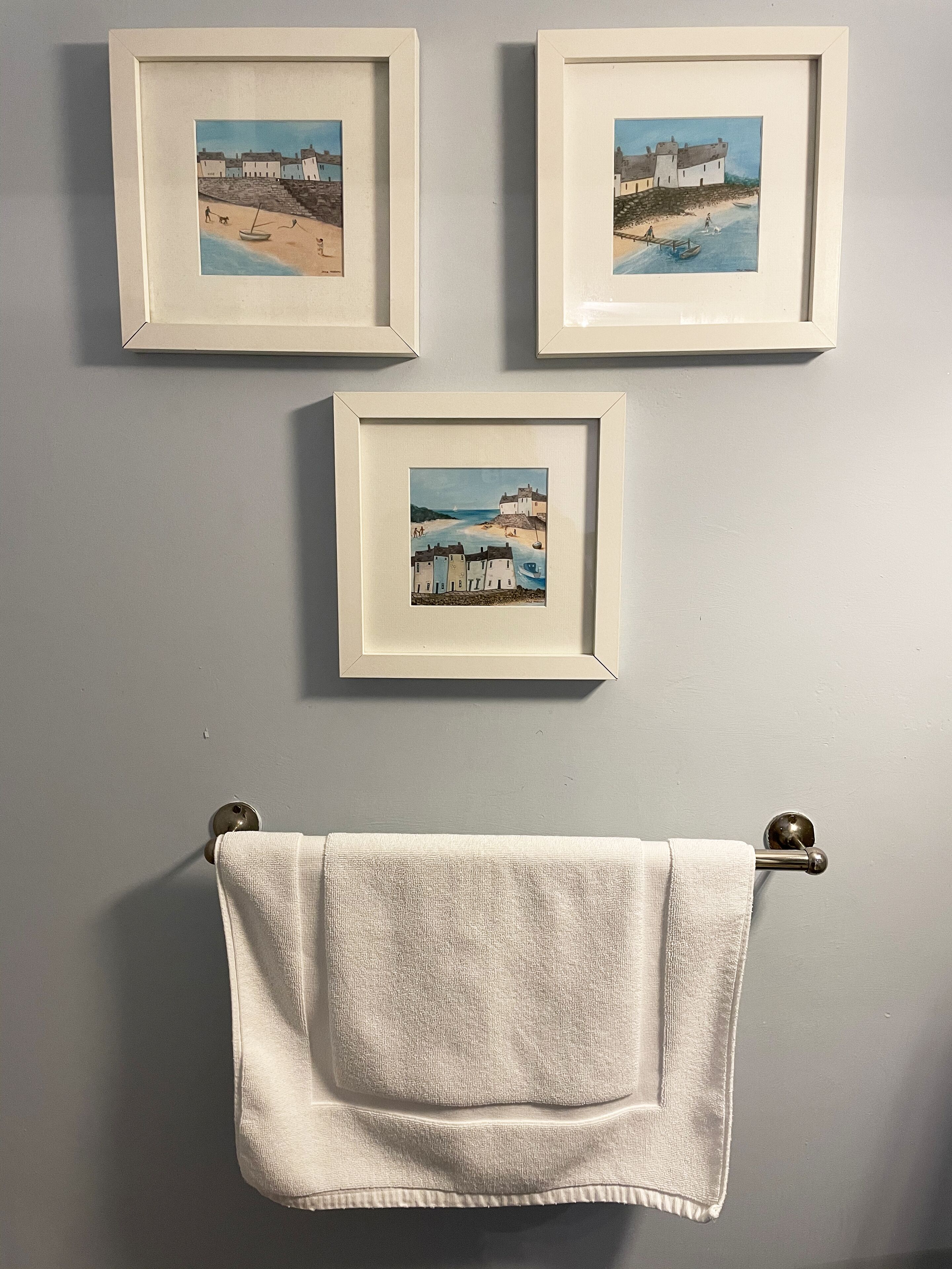 Three framed artworks depicting coastal scenes, a towel hanging on a door, and a door handle.