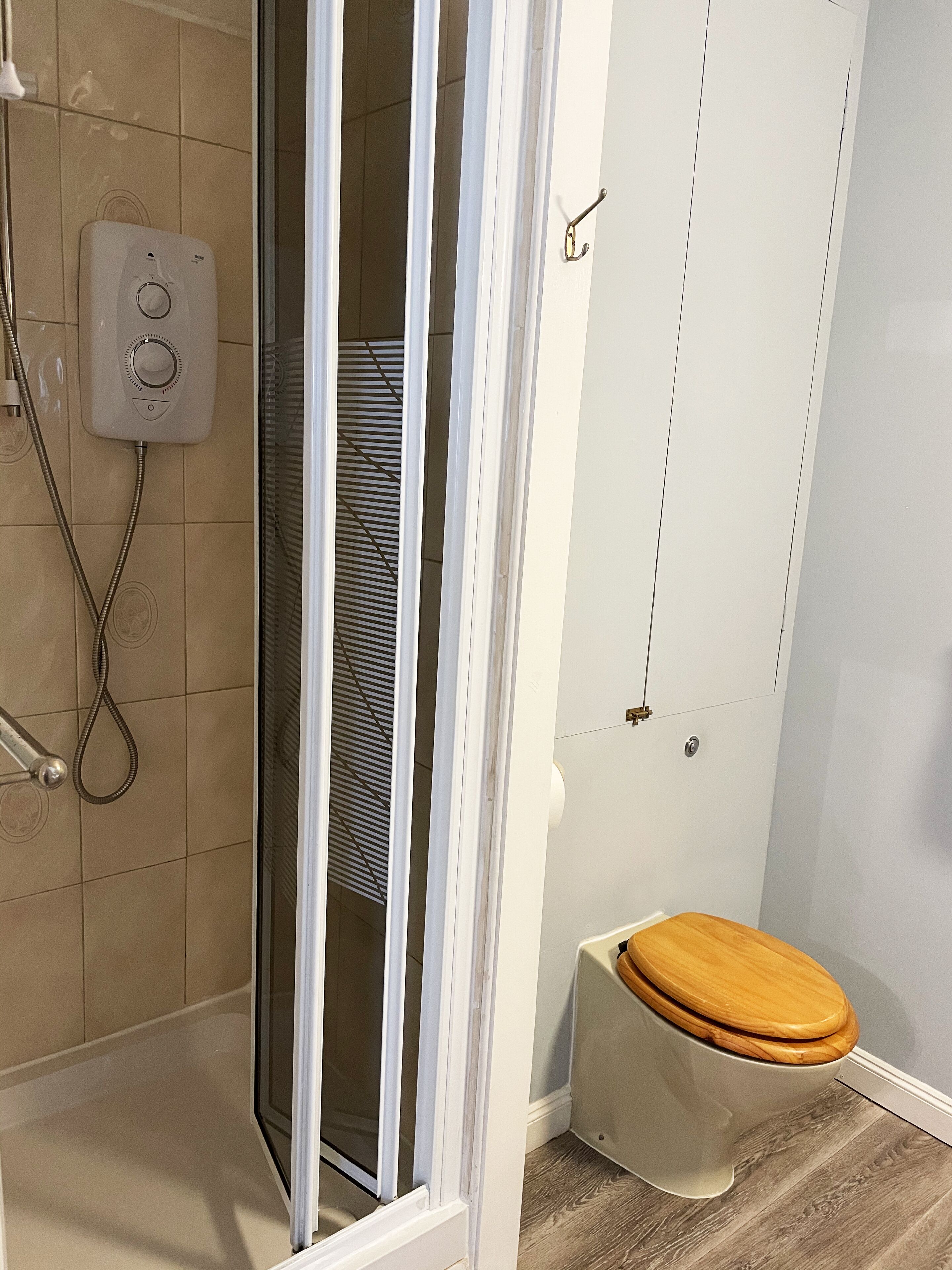 Un bany amb dutxa, vàter i una porta que dona a una altra estança.