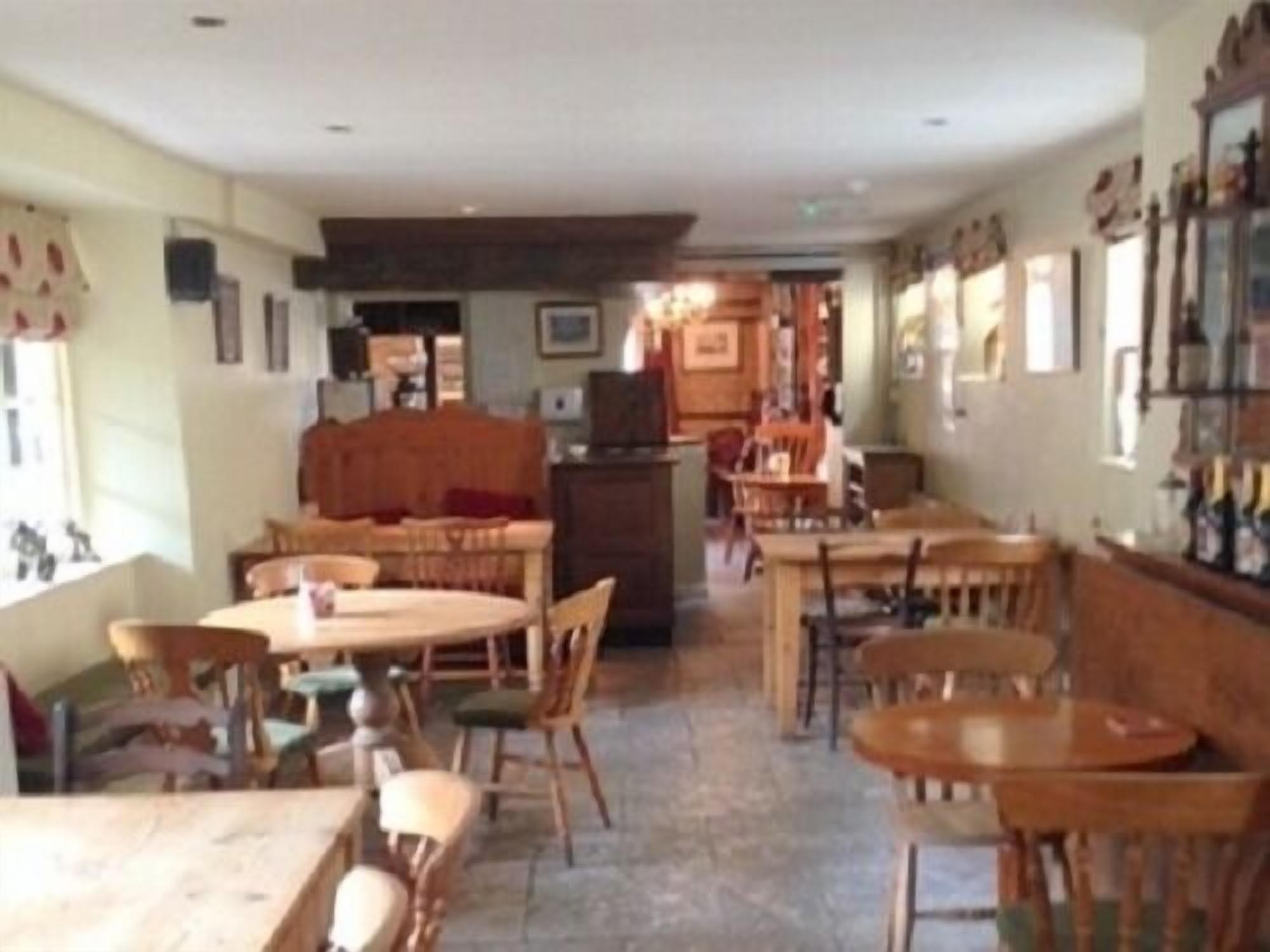 Un comedor con mesas y sillas de madera, una zona de estar central con sofá, y una cocina al fondo.