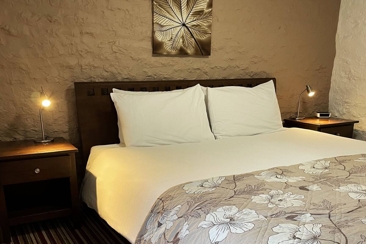 A bedroom with a large bed, two bedside tables with lamps, a textured wall, and a floral-patterned bedspread.