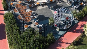 Vista aérea de um hotel com áreas de estar ao ar livre, uma estrutura em cúpula central e vista para o mar.