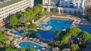 Un resort con varias piscinas, un edificio grande con una torre de reloj y abundante vegetación.