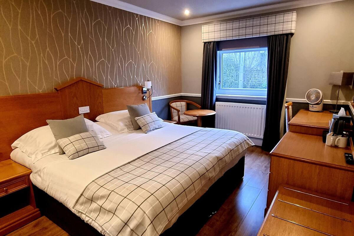 A neatly arranged hotel room with a large bed, bedside tables, a small desk, and a window with curtains.