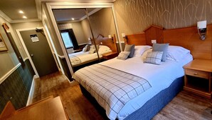 Camera d'albergo con due letti, una testiera in legno, un tavolino e uno specchio.