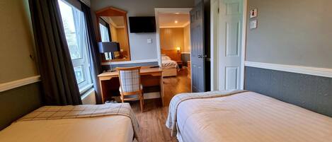 A hotel room with two beds, a desk with a chair, a television, and a door leading to another room.