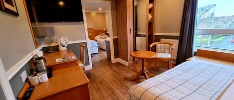 A hotel room with a bed, a desk, a chair, a small table, a TV, and a window with a view of the outside.