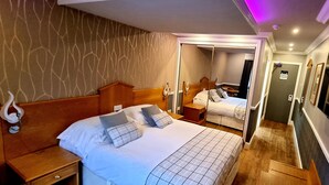 Una camera d'albergo con un letto grande, un comodino, uno specchio e un televisore fissato alla parete.