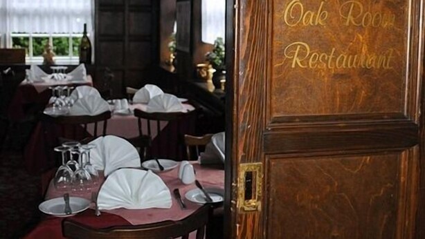 A dining area with tables set for service, a wooden door with "Oak Room Restaurant" engraved on it, and a window with a view of greenery outside. - Ye Olde Red Lion (York)