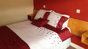 A bed with a red and white bedspread, two pillows, and a wooden headboard. - Ye Olde Red Lion (York)