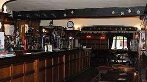 A bar with wooden paneling, a clock, and a bar counter with stools. - Ye Olde Red Lion (York)
