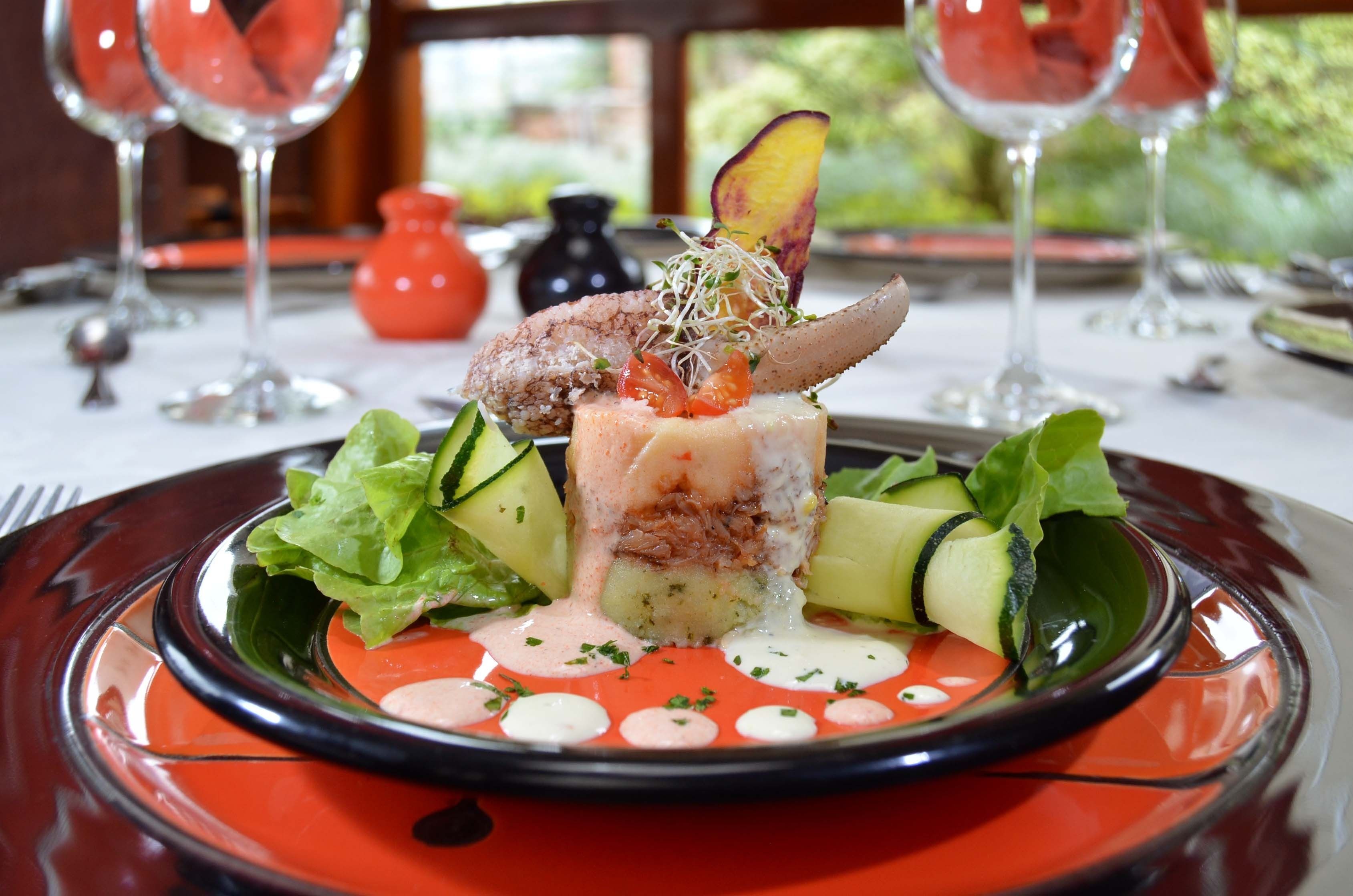 A plated dish with a variety of vegetables and a decorative element on top, set on a table with a red and black plate.