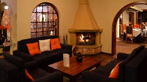 A cozy lounge area with a fireplace, comfortable seating, and a view through a window. - Hosteria Durán (Banos)