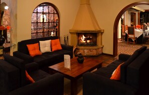 A cozy lounge area with a fireplace, comfortable seating, and a view through a window. - Hosteria Durán (Banos)
