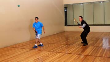 Uma quadra de squash com piso de madeira e parede de vidro.