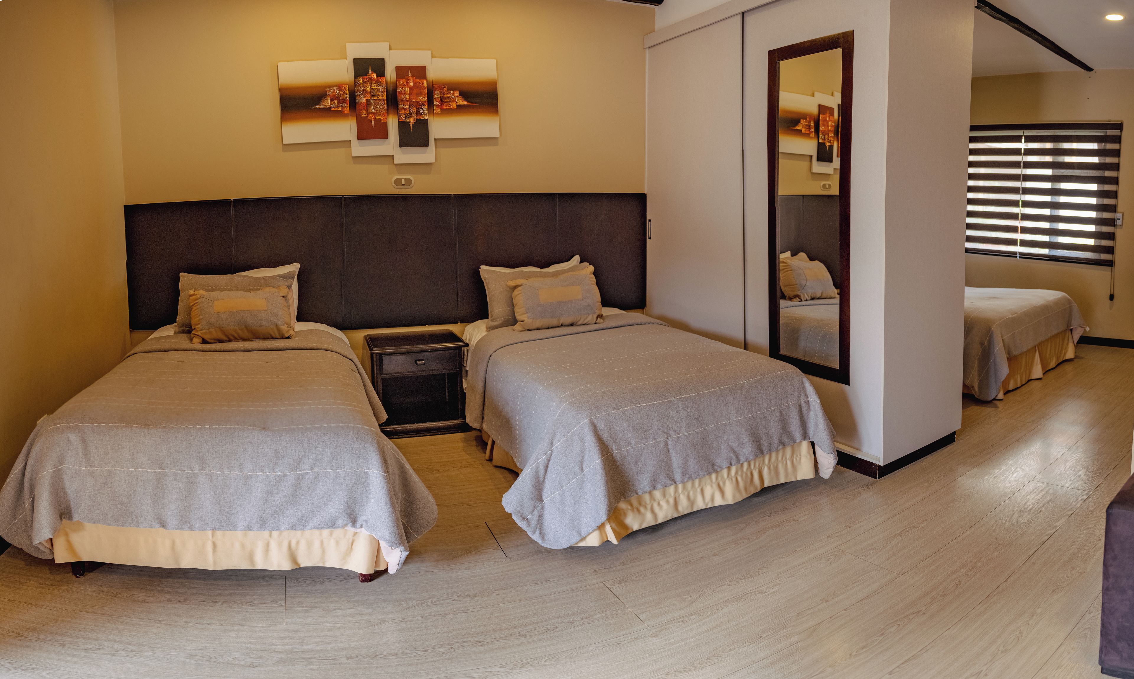 A hotel room with two beds, a nightstand, a mirror, and a wall-mounted artwork.