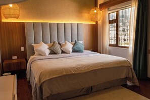 Une chambre à coucher avec un grand lit, une tête de lit, des tables de chevet et une fenêtre avec des rideaux.