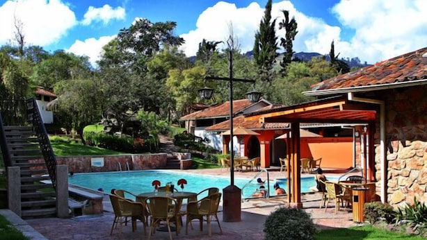 A pool area with a stone wall, outdoor seating, and a covered patio. - Hosteria Durán (Banos)