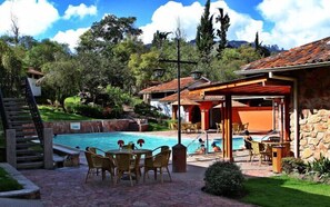 A pool area with a stone wall, outdoor seating, and a covered patio. - Hosteria Durán (Banos)