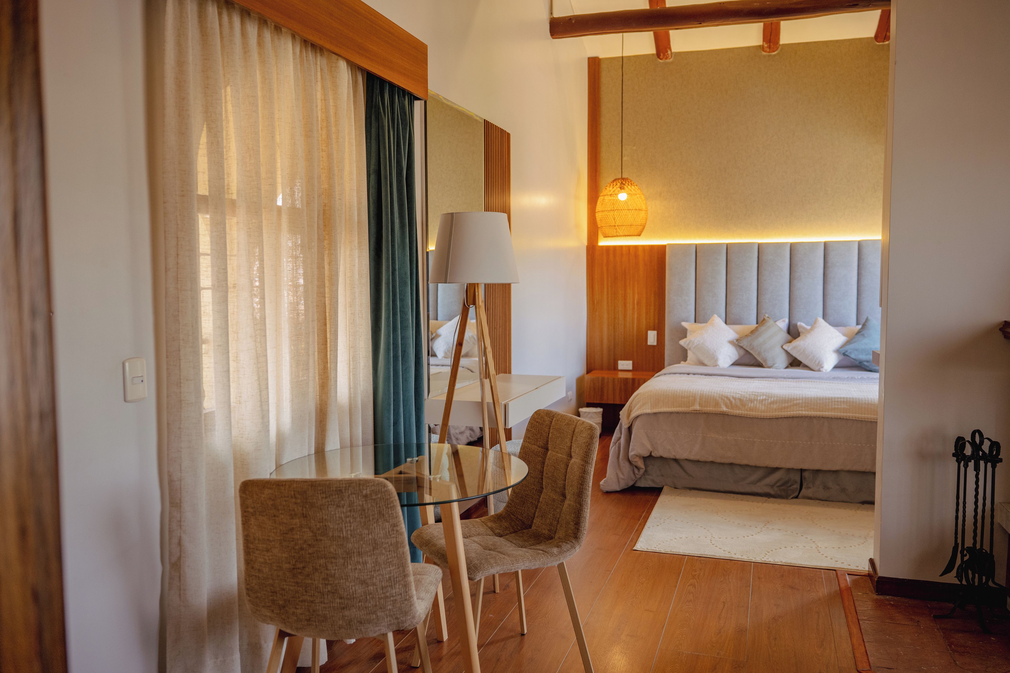 Habitación de hotel con cama, escritorio, silla, lámpara y ventana grande con cortinas.
