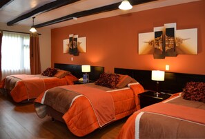 A hotel room with two beds, each with an orange bedspread and matching pillows. There are two bedside tables with lamps, and the walls are adorned with framed artwork. - Hosteria Durán (Banos)
