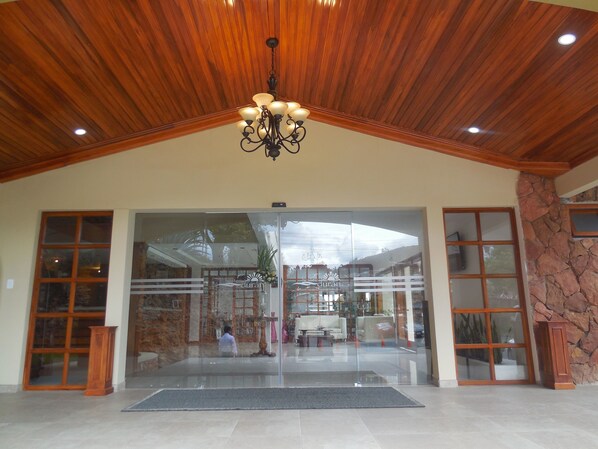 A hotel lobby with a wooden ceiling, a chandelier, large glass doors, and a stone wall. - Hosteria Durán (Banos)